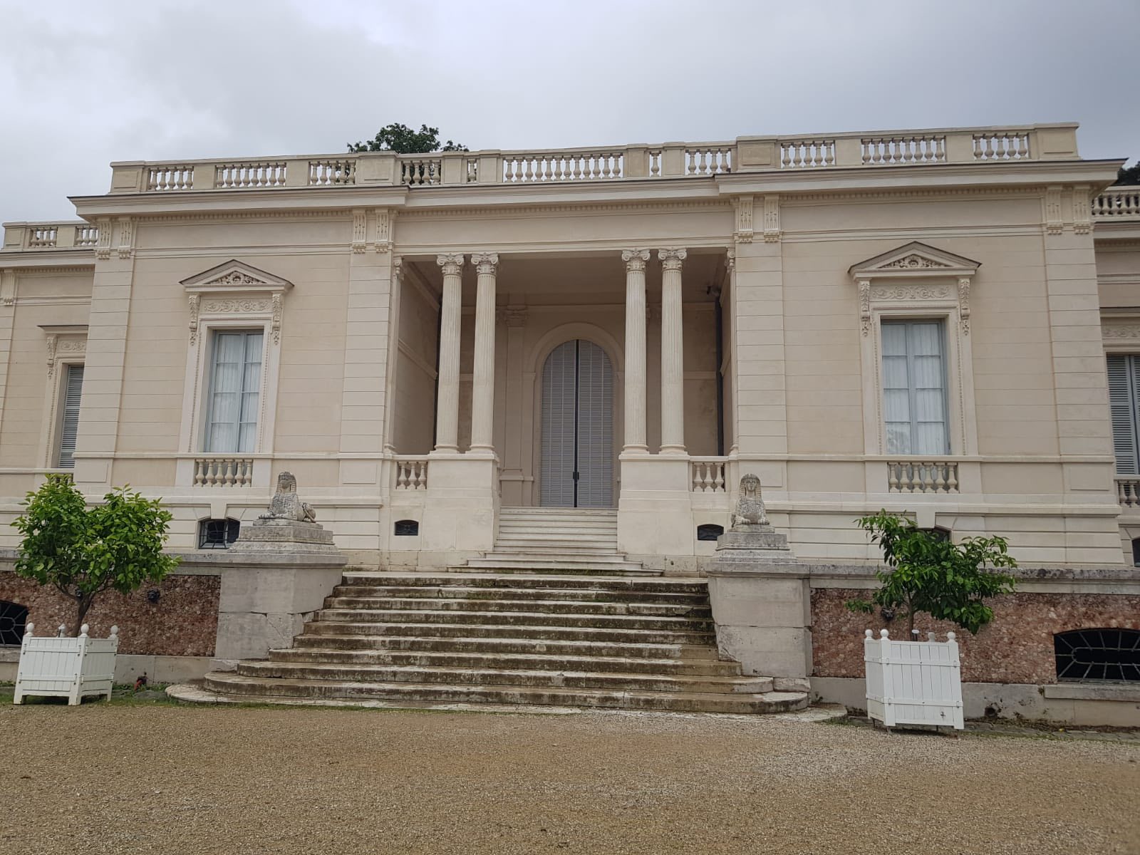 712429299_1290691929885297_8178209169252527041_n Beige neoclassical mansion facade with tall columns and arched doorway, stone steps, and decorative window pediments.