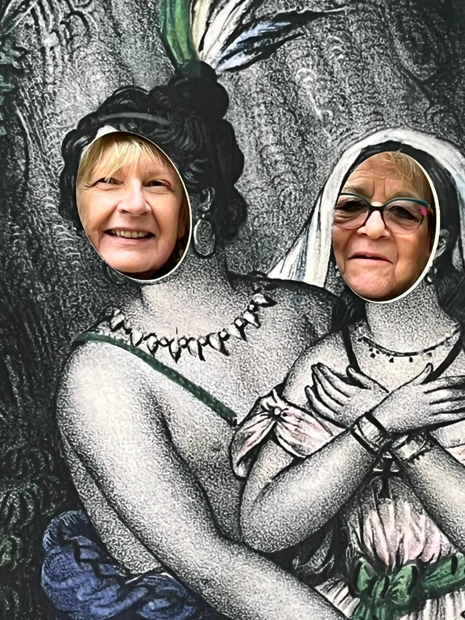 715990165_1291534573134366_7322736347966043963_n Two smiling women poke their faces through cutouts in a large black-and-white dinosaur mural, posing playfully.