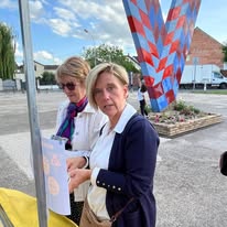 721223790_1299411779013312_9064924129182624794_n Two women stand outdoors by a yellow ballot drop box; one is inserting a ballot while the other watches on a sunny day.