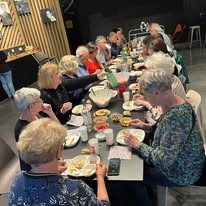 721465997_1297871835833973_8890823005443359925_n Group of seniors sitting at a long table sharing a meal in a community center. (informative)