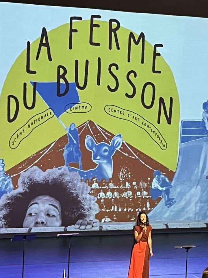 724076806_1300185322269291_4776273923700150340_n Colorful mural advertising La Ferme Du Buisson with mountains, animals, and text in a bright circle; a singer stands on stage in front of it.