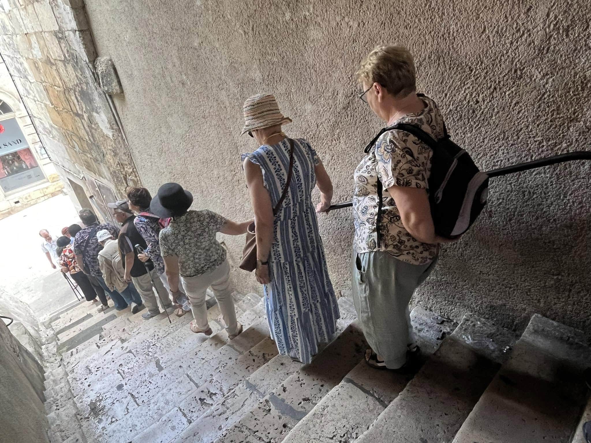 726447865_1305292801758543_8514845833267239615_n Tour group standing on a stone stairway inside a historic site, wearing hats and backpacks as they look ahead.