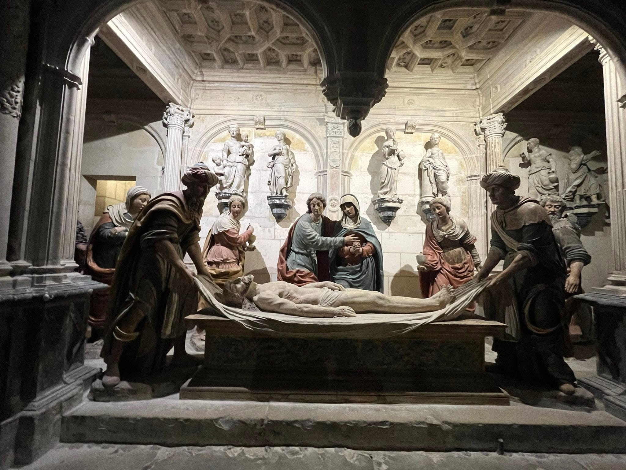 726575667_1305298601757963_7555133281894106338_n Religious sculptural scene: mourners gather around a central bier with Jesus' body, in a dimly lit hall with arches and statues in the background.