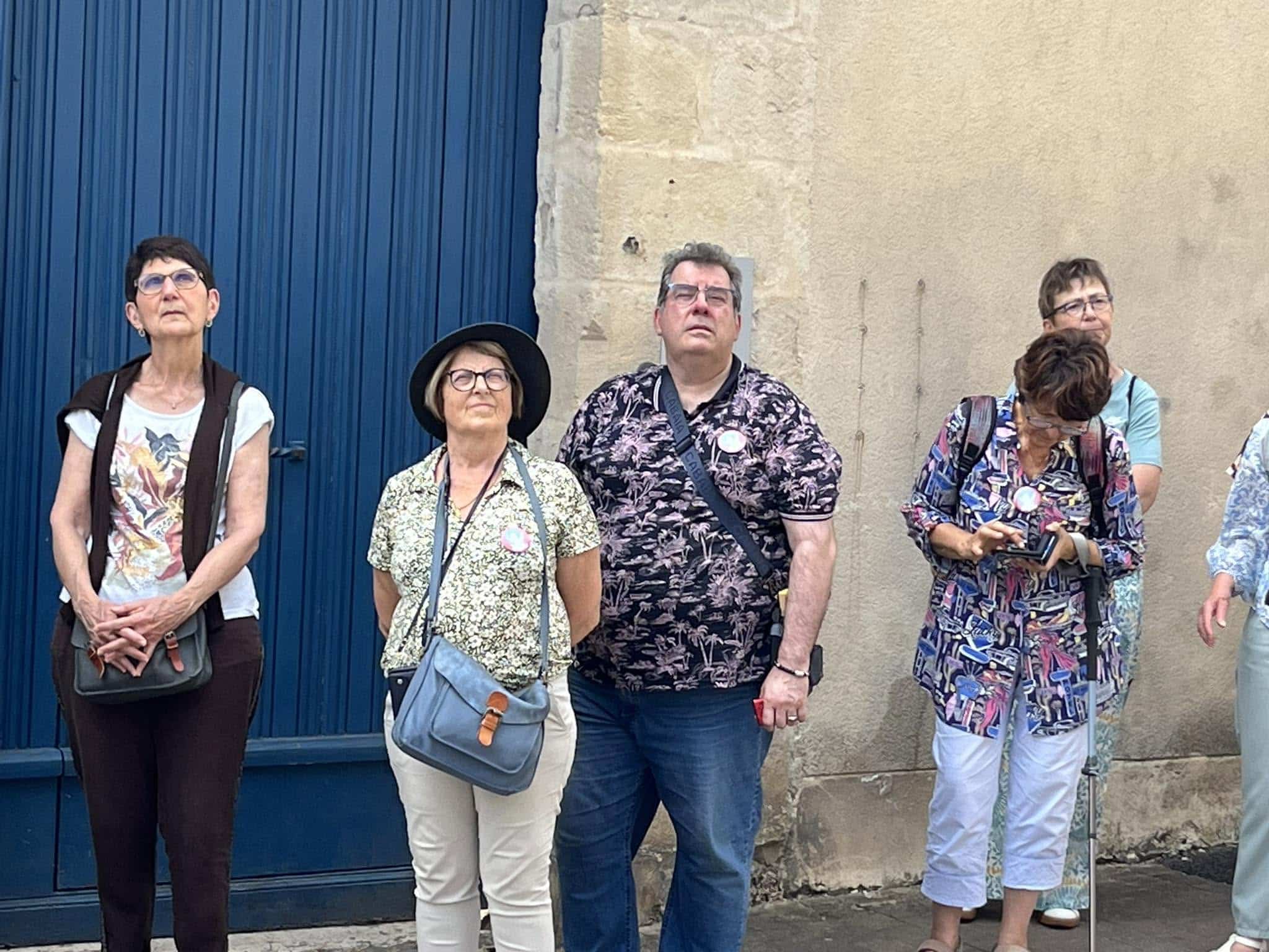 726607061_1305290285092128_6309579885469440207_n Six adults stand in a row outdoors, posing in front of a blue door and beige wall.
