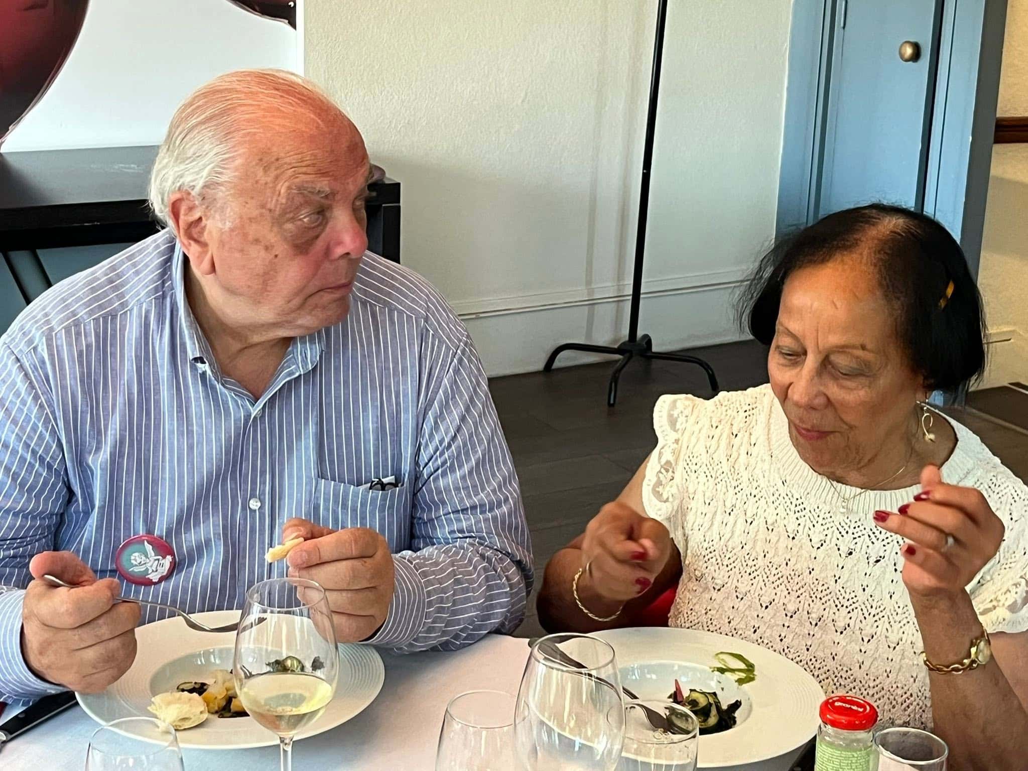 727498075_1305299945091162_7433324254460178739_n Two seniors at a table sharing a meal, chatting as they eat small bites and sip from stemmed glasses.