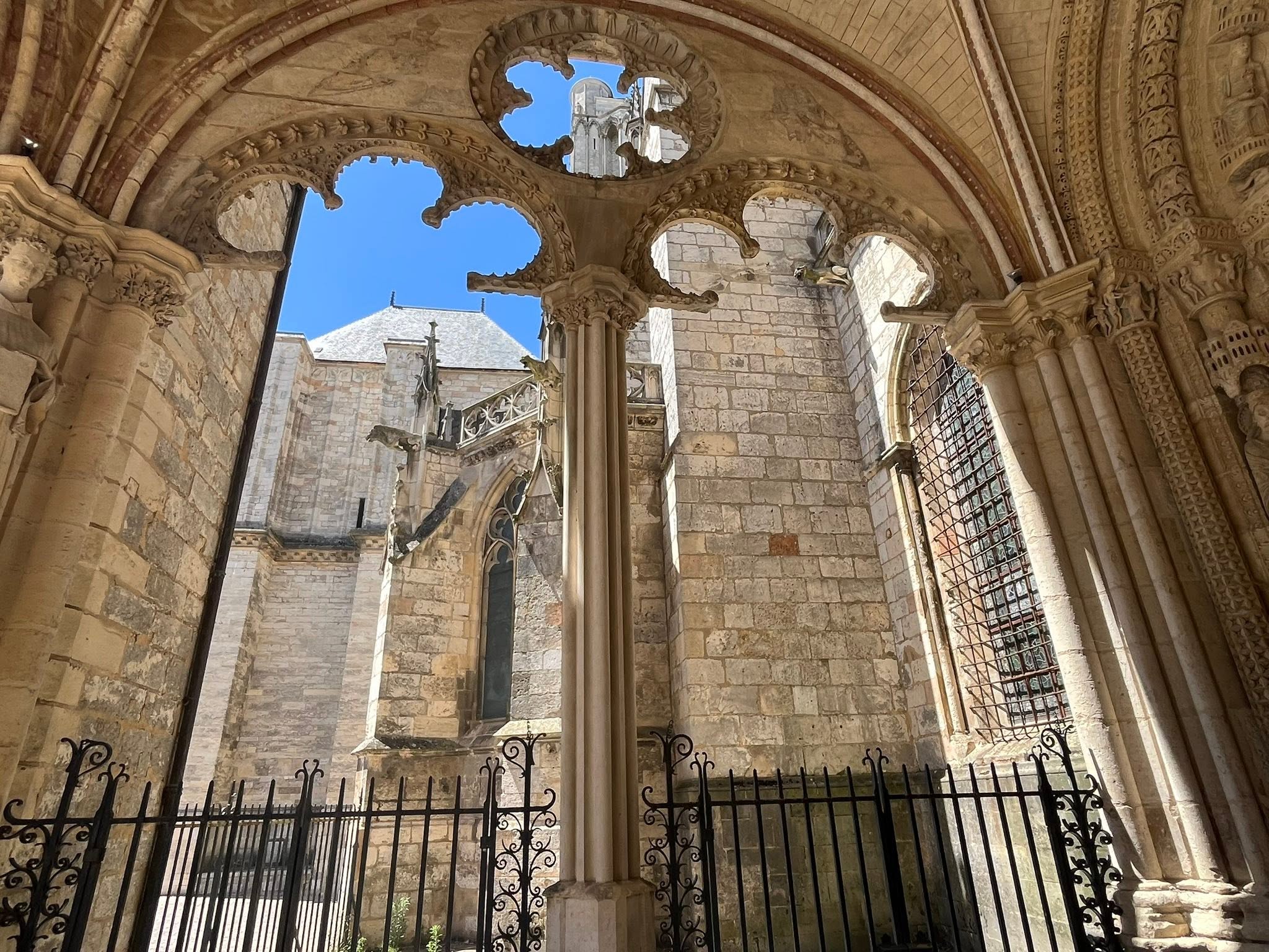727519482_1305297805091376_4417301284375619122_n Interior of a medieval stone cathedral with ornate arches, carved columns, and a blue sky visible through decorative openings above a barred window boundary.