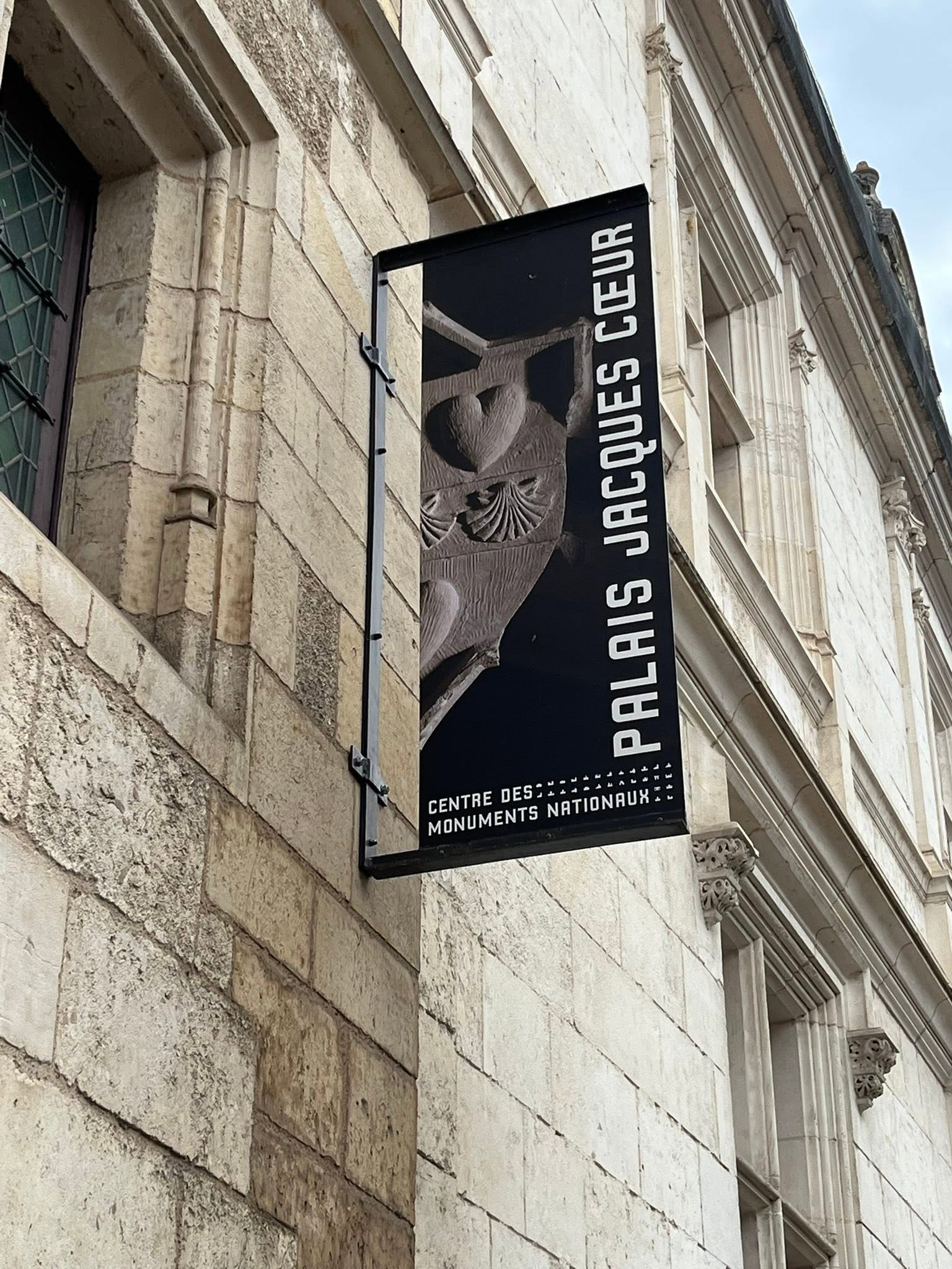 727519965_1306129988341491_8224054615004166715_n Vertical black sign on a historic stone building reading 'Centre des Monuments Nationaux' with decorative carvings on the facade.