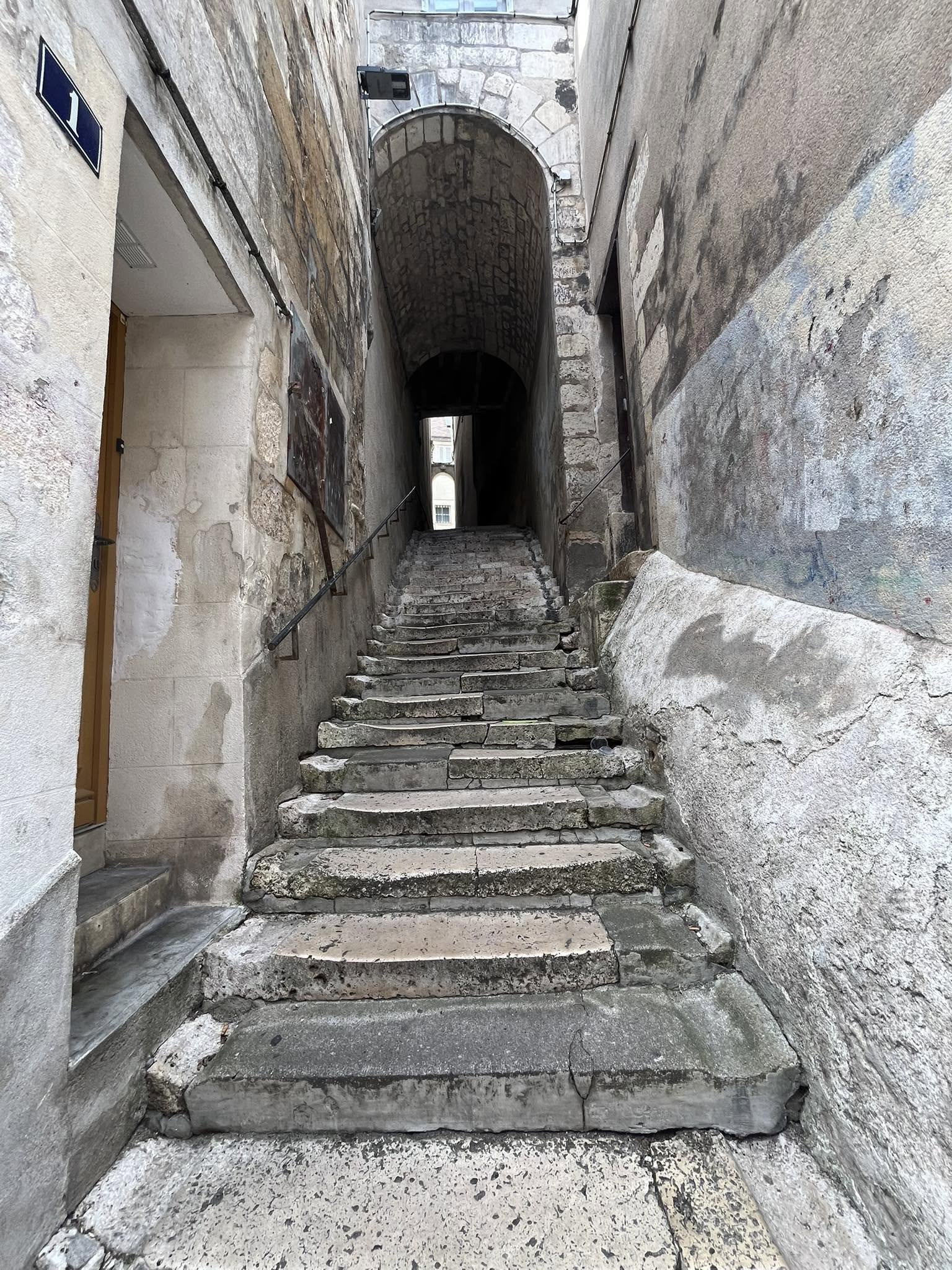 727885028_1305292061758617_1067441071134923237_n Narrow stone alley with worn walls and weathered steps leading up to a stone archway.