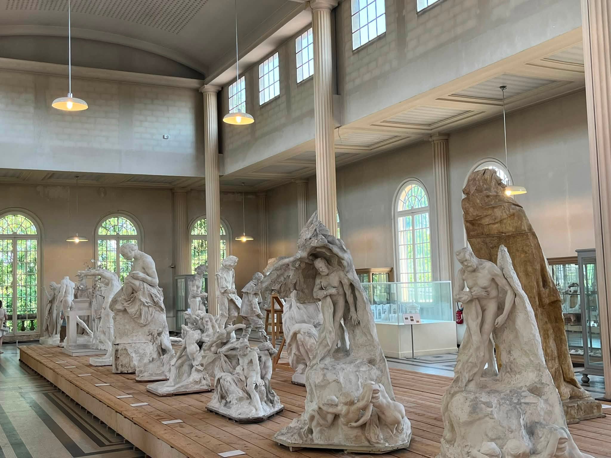 741901440_1322793160008507_3718651397534161990_n White marble statue figures arranged on a wooden platform inside a classical-style museum hall with tall columns and arched windows