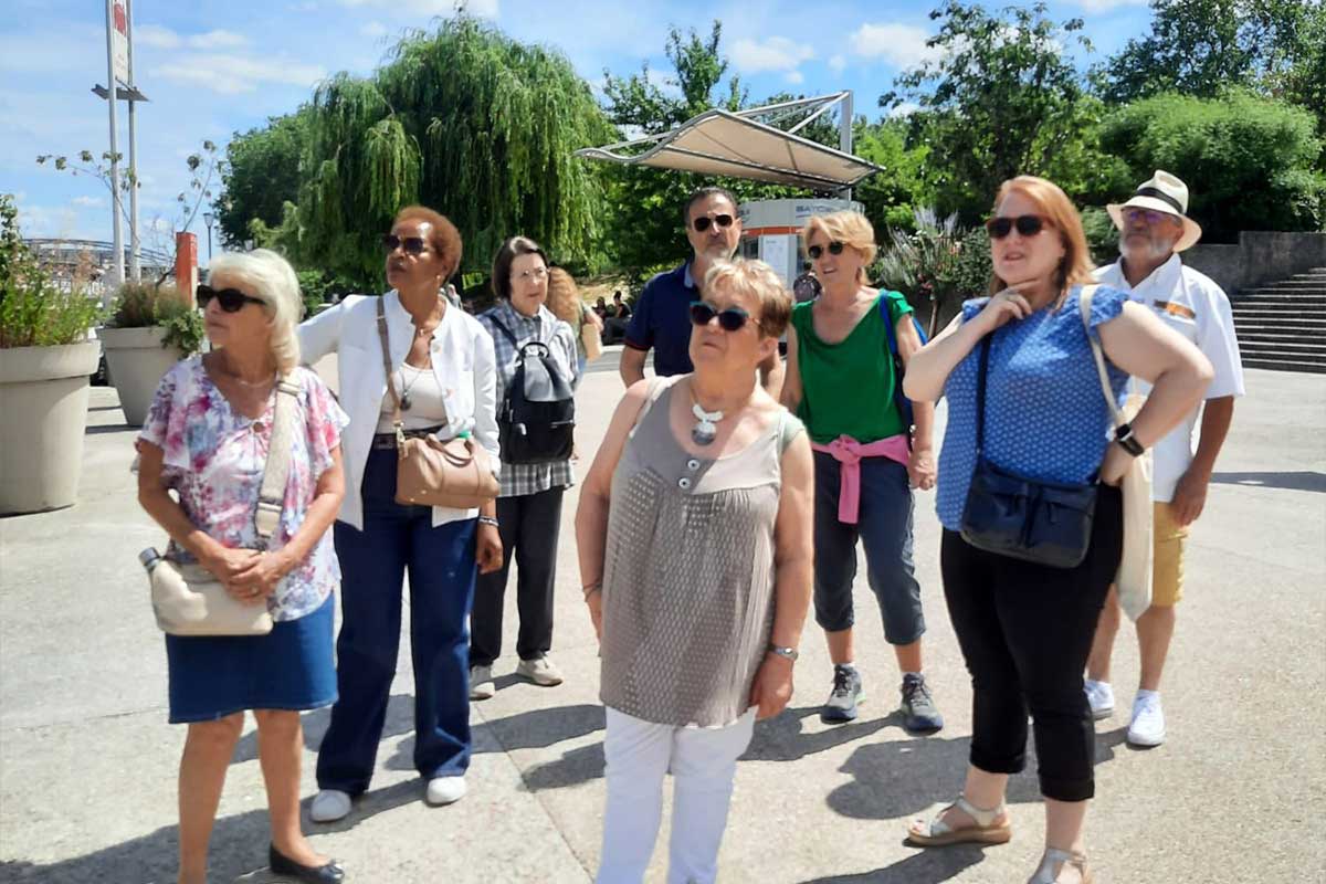 Group of senior tourists standing outdoors on a sunny day, wearing casual clothes and sunglasses, looking in a common direction.